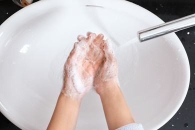 Woman washing hands with soap over sink in bathroom, top view