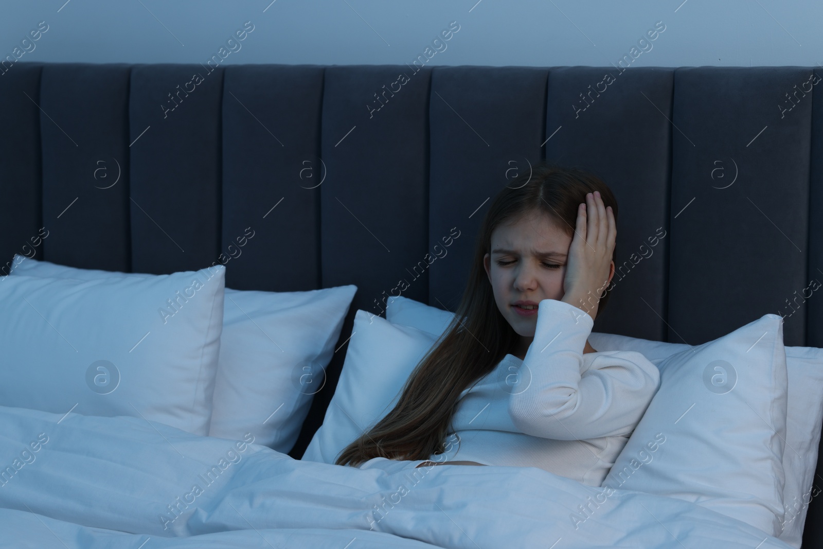 Photo of Little girl suffering from headache in bed at night