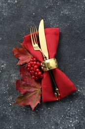 Photo of Thanksgiving table setting. Cutlery, napkin, autumn leaves and berries on black background, flat lay