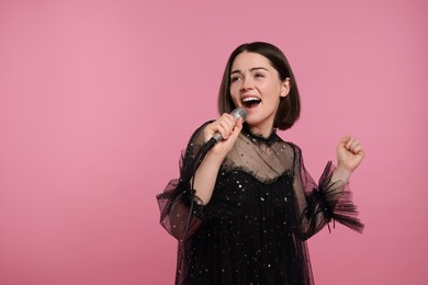 Photo of Beautiful young woman with microphone singing on pink background, space for text