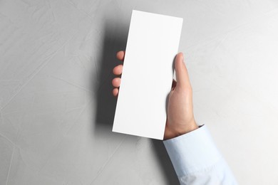 Photo of Man holding white blank card at light grey table, top view. Mockup for design