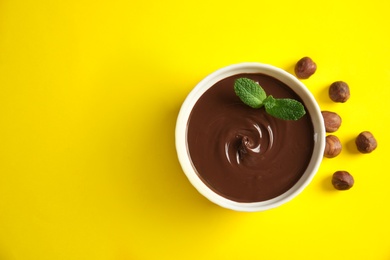 Dessert bowl with sweet chocolate cream, hazelnuts and mint on color background, top view. Space for text