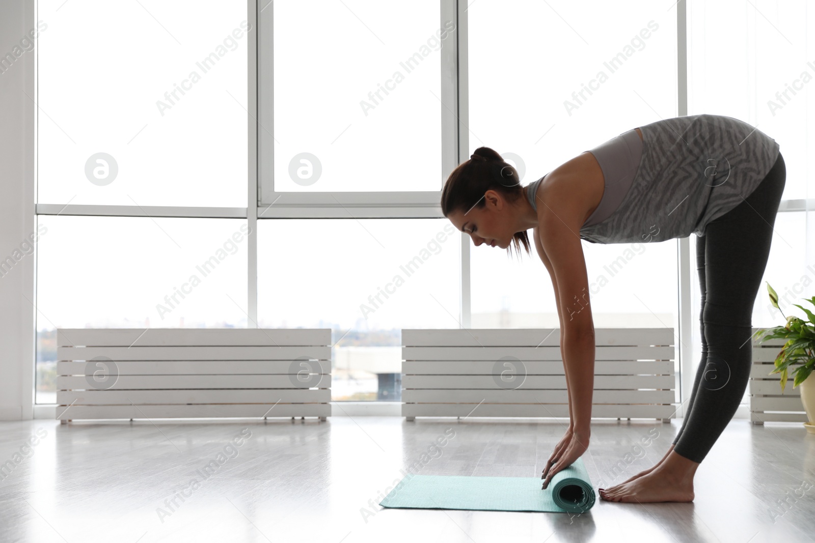 Photo of Young woman unrolling mat in yoga studio