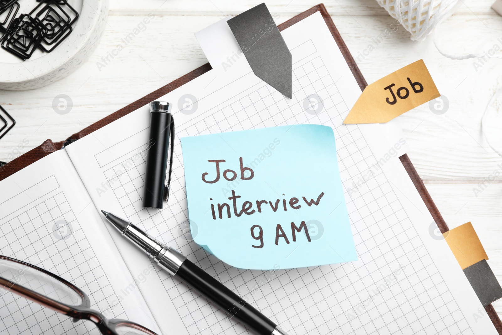 Photo of Reminder note about job interview and stationery on table, flat lay