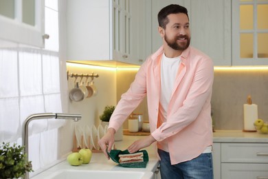 Man packing sandwich into beeswax food wrap at countertop in kitchen