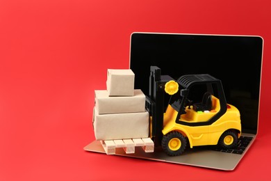Photo of Laptop, toy forklift with wooden pallet and boxes on red background, space for text