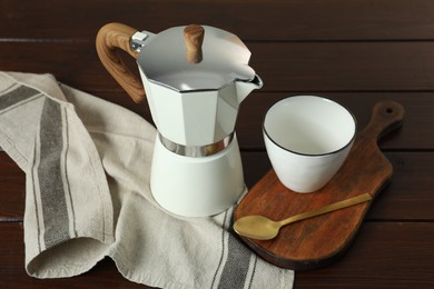 Moka pot, spoon, cup and kitchen towel on wooden table