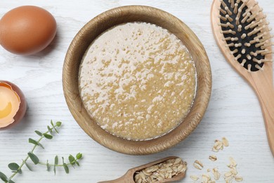 Homemade hair mask in bowl, ingredients and brush on white wooden table, flat lay