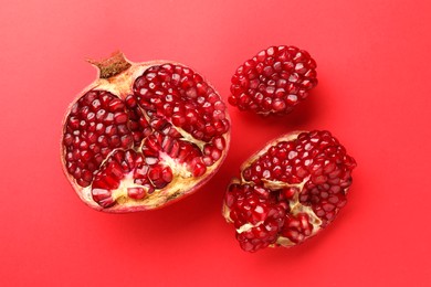 Photo of Whole and cut fresh pomegranates on red background, flat lay