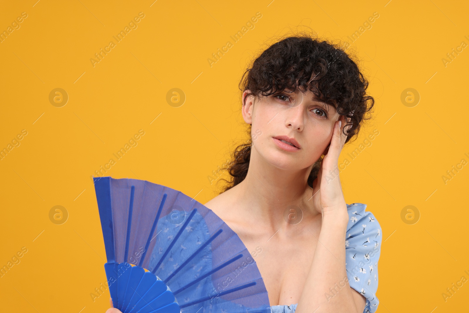 Photo of Woman with hand fan suffering from heat on orange background