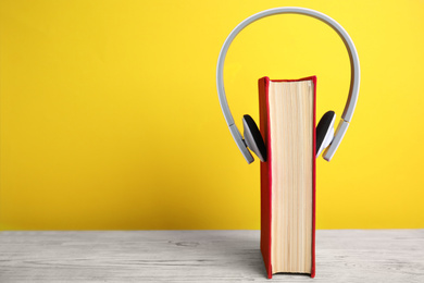 Book and modern headphones on white wooden table against yellow background. Space for text