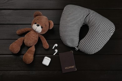 Photo of Striped travel pillow, toy bear, passport and earphones on dark wooden background, flat lay