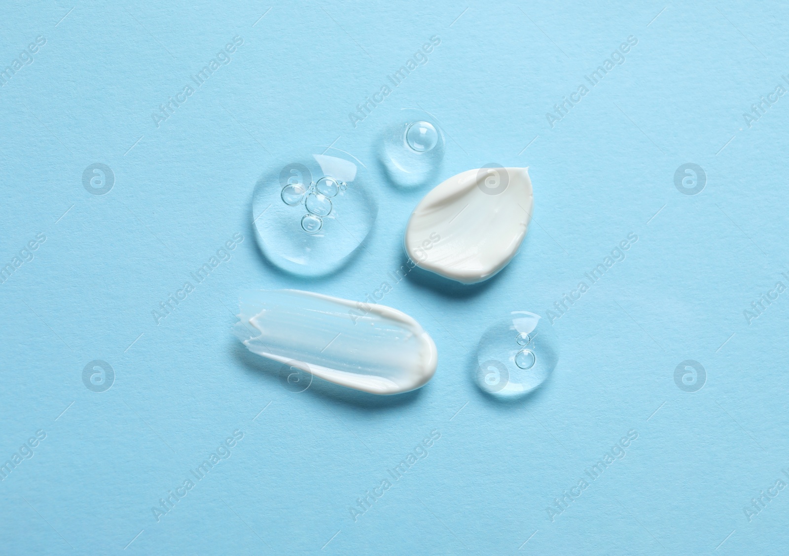 Photo of Samples of transparent gel and white cream on light blue background, flat lay