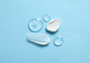 Photo of Samples of transparent gel and white cream on light blue background, flat lay