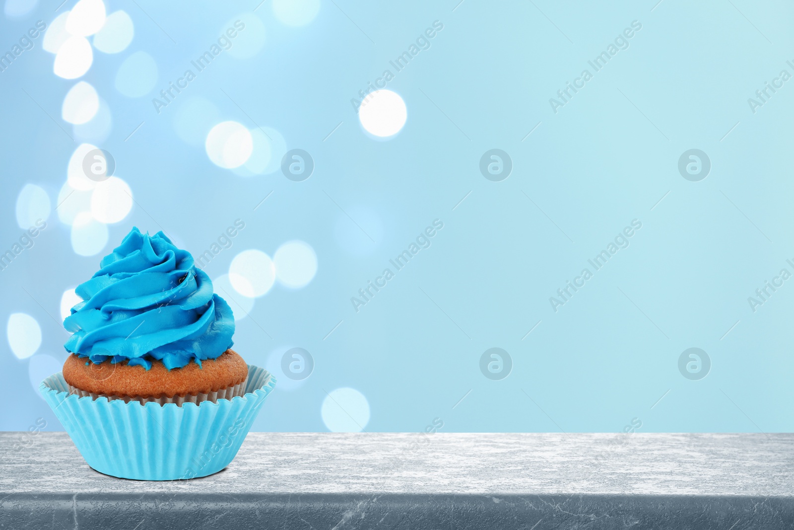 Image of Delicious birthday cupcake on grey table against blurred lights. Space for text