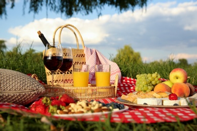 Picnic blanket with delicious food and drinks on green grass