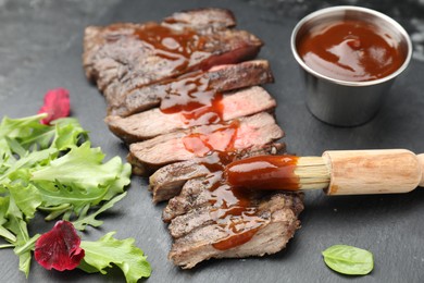 Pieces of delicious roasted beef meat with sauce and greens on black table, closeup