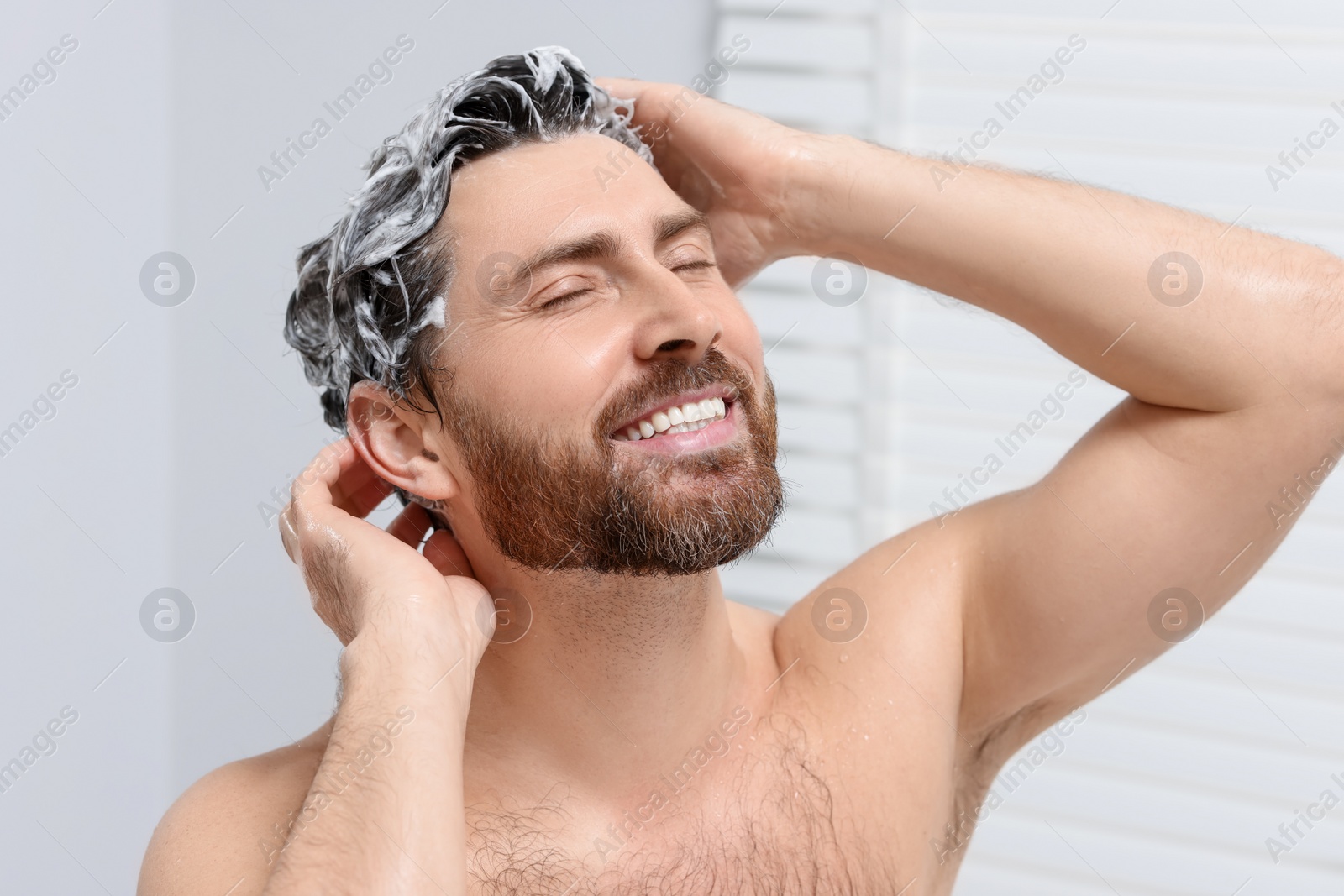 Photo of Happy man washing his hair with shampoo in shower