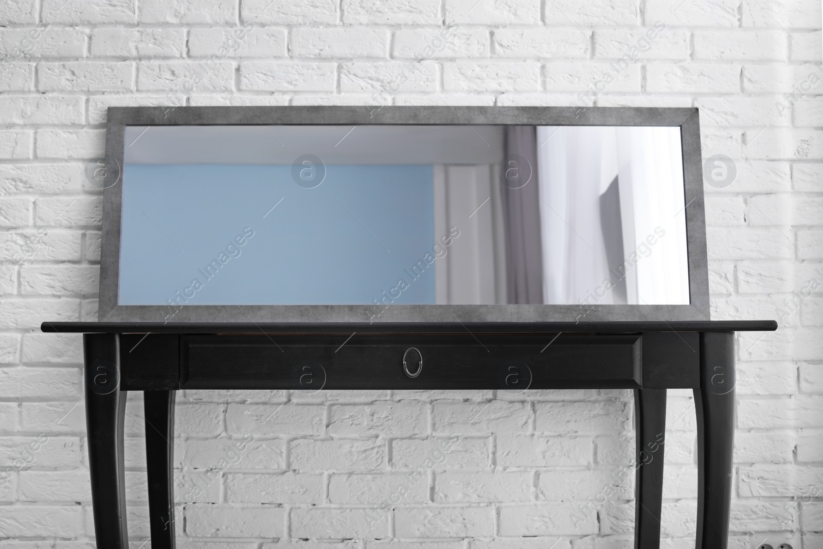 Photo of Modern mirror on table near brick wall