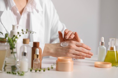 Photo of Dermatologist applying cream onto hand at white table indoors, closeup. Testing cosmetic product