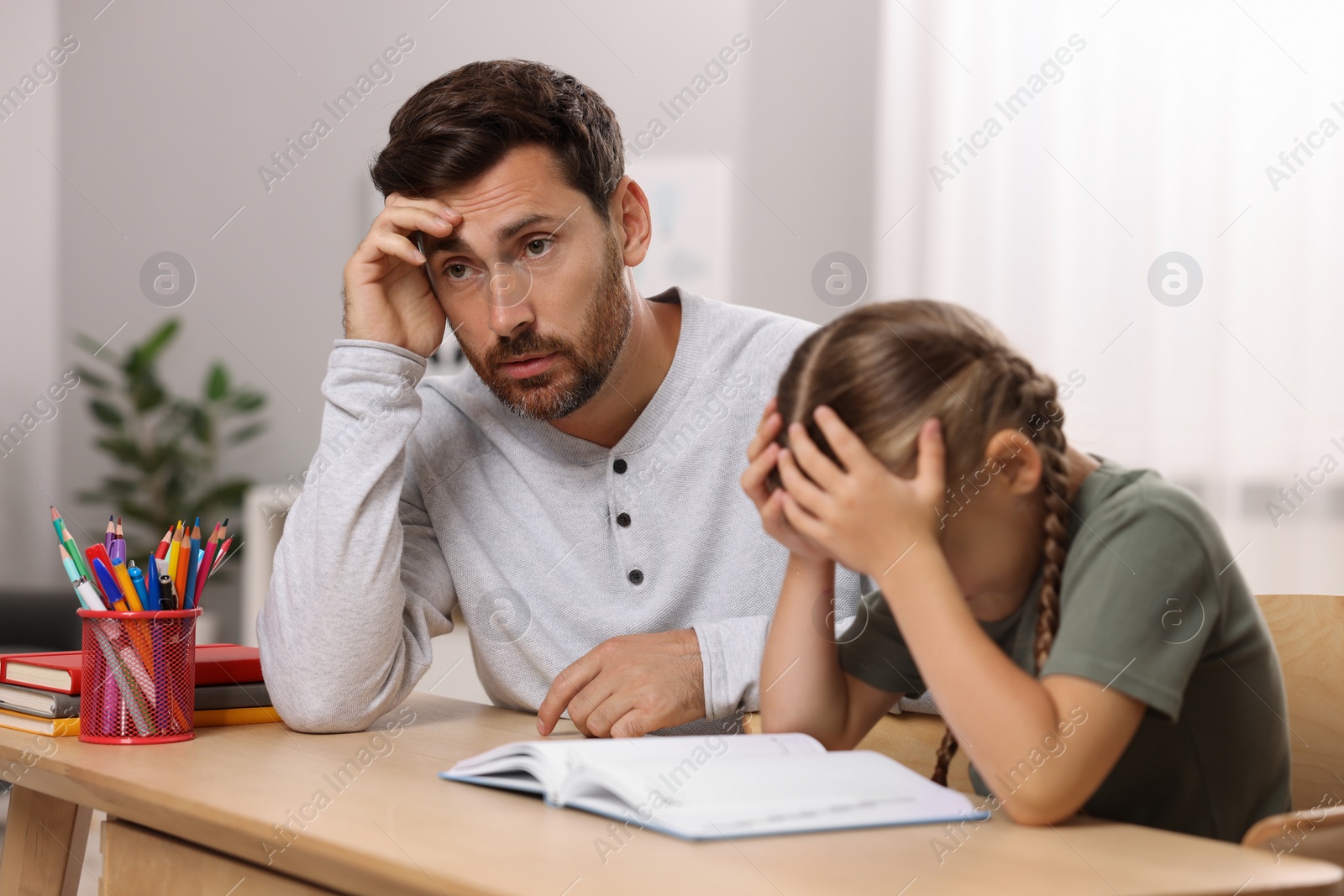 Photo of Dyslexia problem. Bored father helping daughter with homework at table in room, selective focus