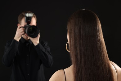 Photo of Professional photographer taking picture of model on black background, selective focus
