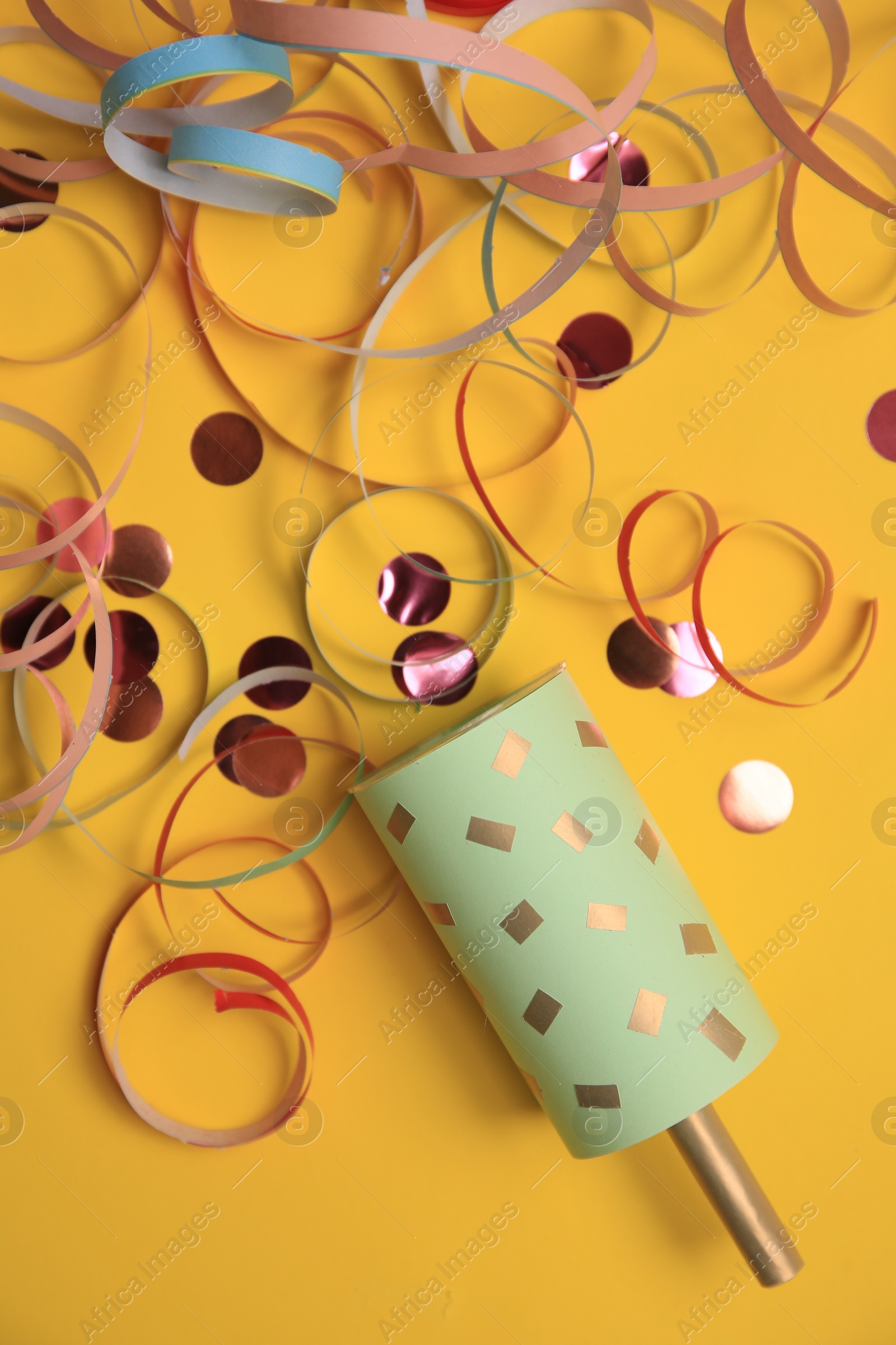 Photo of Beautiful serpentine and confetti bursting out of party popper on orange background, flat lay