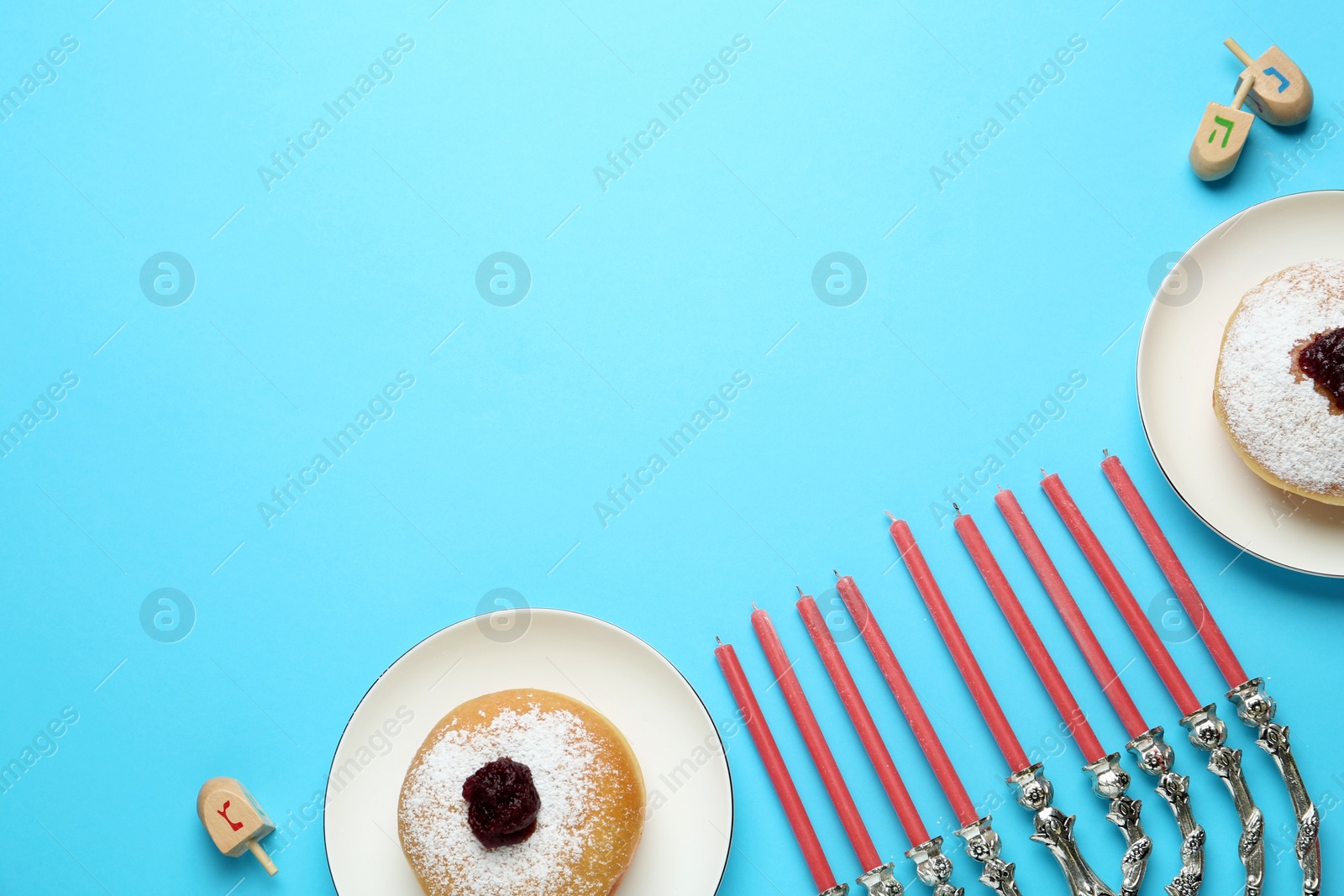 Photo of Hanukkah traditional menorah, candles, doughnuts, dreidels with letters He, Pe, Nun, Gimel on light blue background, flat lay. Space for text