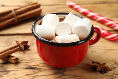 Photo of Tasty hot chocolate with marshmallows, candy cane and spices on wooden table, closeup