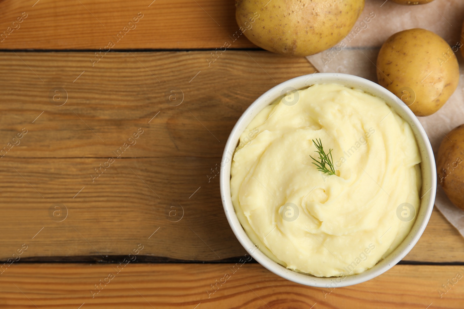 Photo of Freshly cooked homemade mashed potatoes and raw vegetables on wooden table, flat lay. Space for text