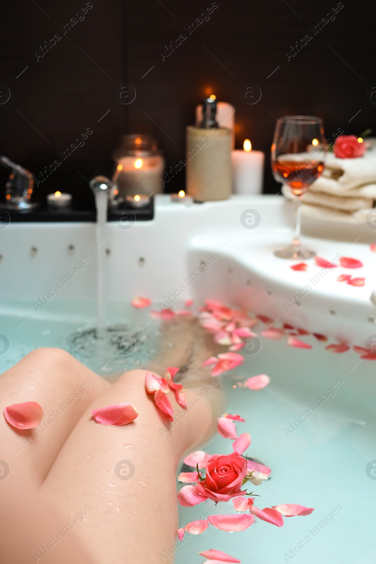 Photo of Woman taking bath with rose petals, closeup. Romantic atmosphere