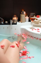 Photo of Woman taking bath with rose petals, closeup. Romantic atmosphere