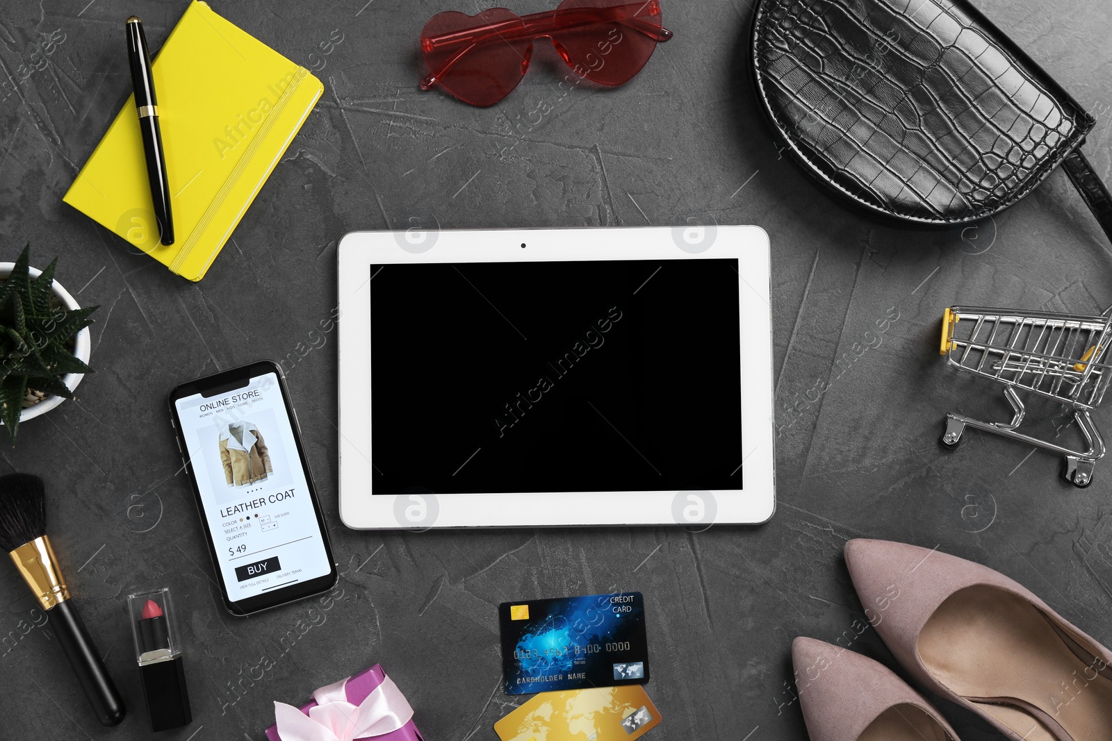 Photo of Online store. Tablet, smartphone, credit cards, stationery, accessories and shopping cart on grey table, flat lay