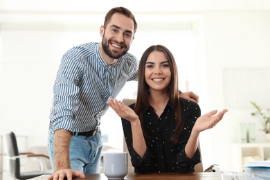 Photo of Happy young couple looking at camera and using video chat in home office