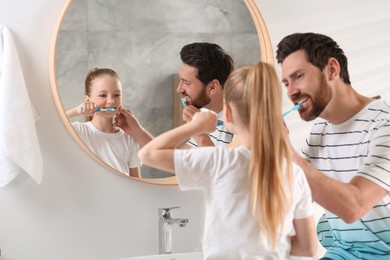 Father and his daughter brushing teeth together near mirror in bathroom