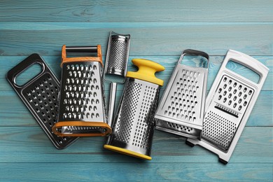 Different modern graters on light blue wooden table, flat lay