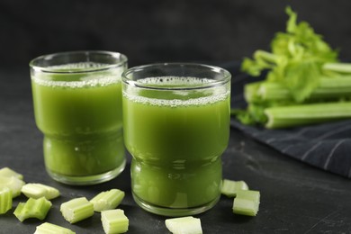Photo of Glasses of delicious celery juice and vegetables on black table, closeup