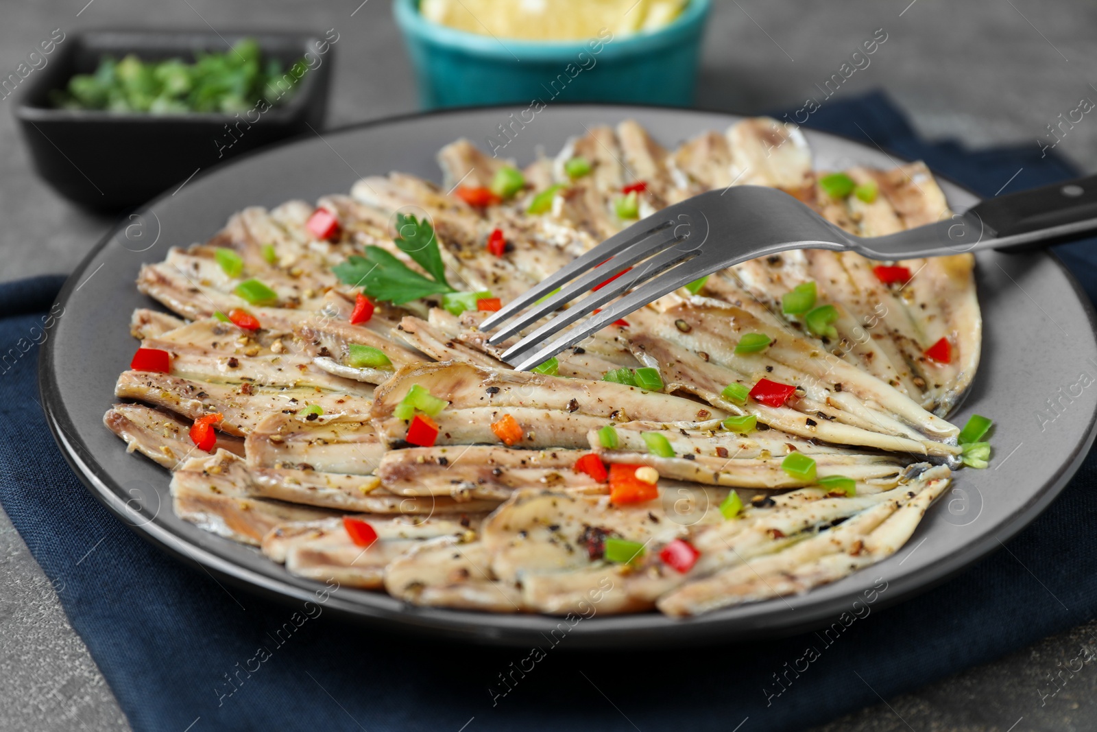 Photo of Tasty pickled anchovies with spices and fork on table, closeup