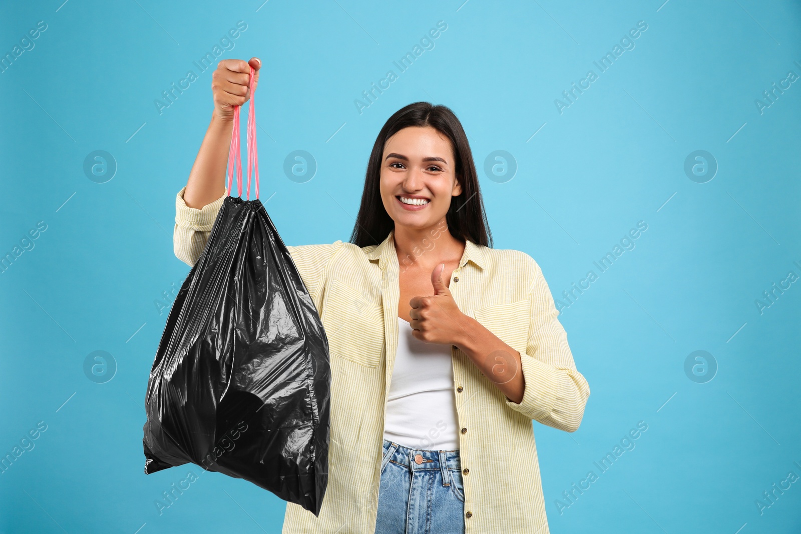 Photo of Woman holding full garbage bag on light blue background