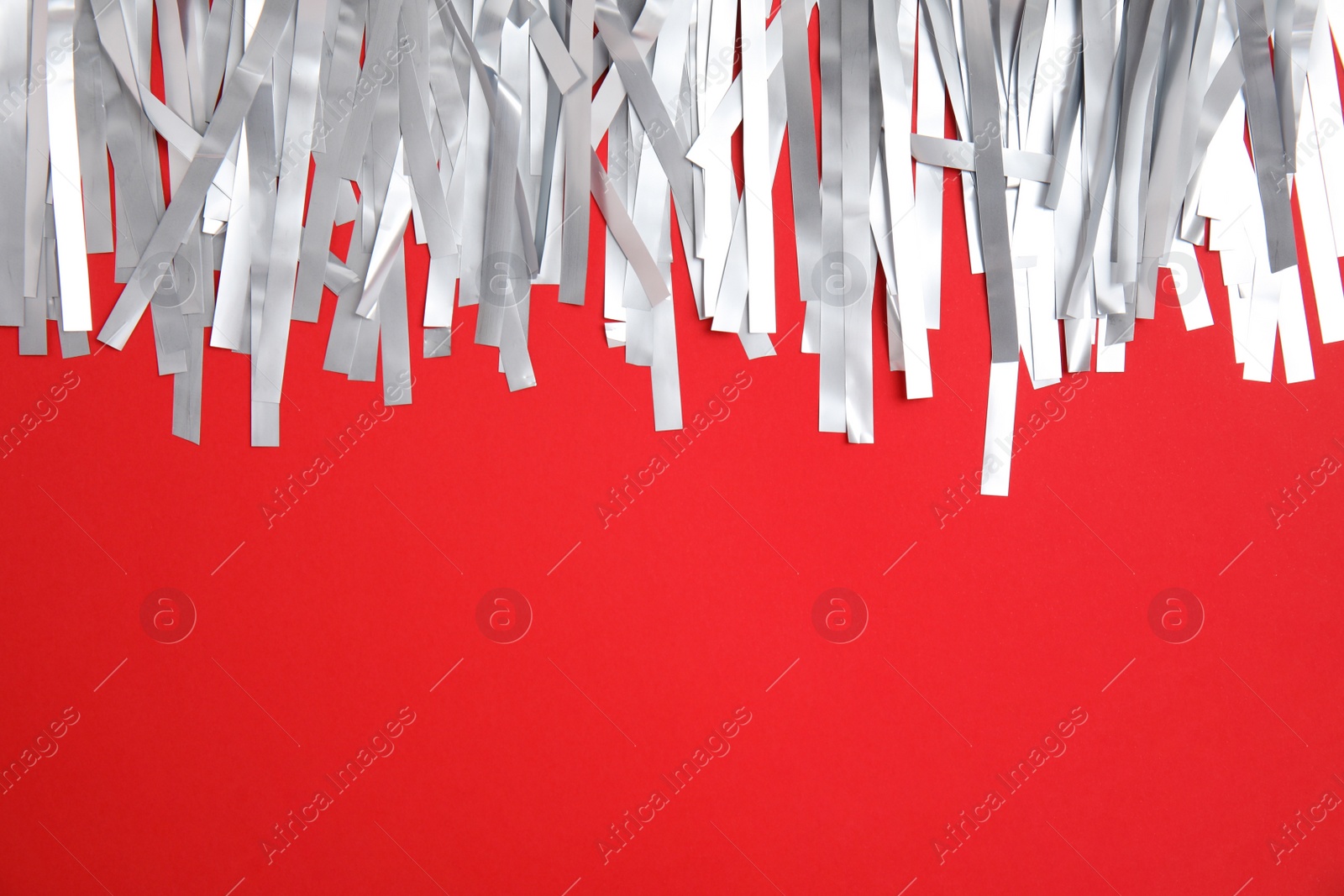 Photo of Silver tinsel on red background, top view. Space for text