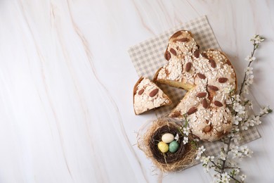 Photo of Delicious Italian Easter dove cake (traditional Colomba di Pasqua), decorative nest with painted eggs and flowering branches on white table, flat lay. Space for text