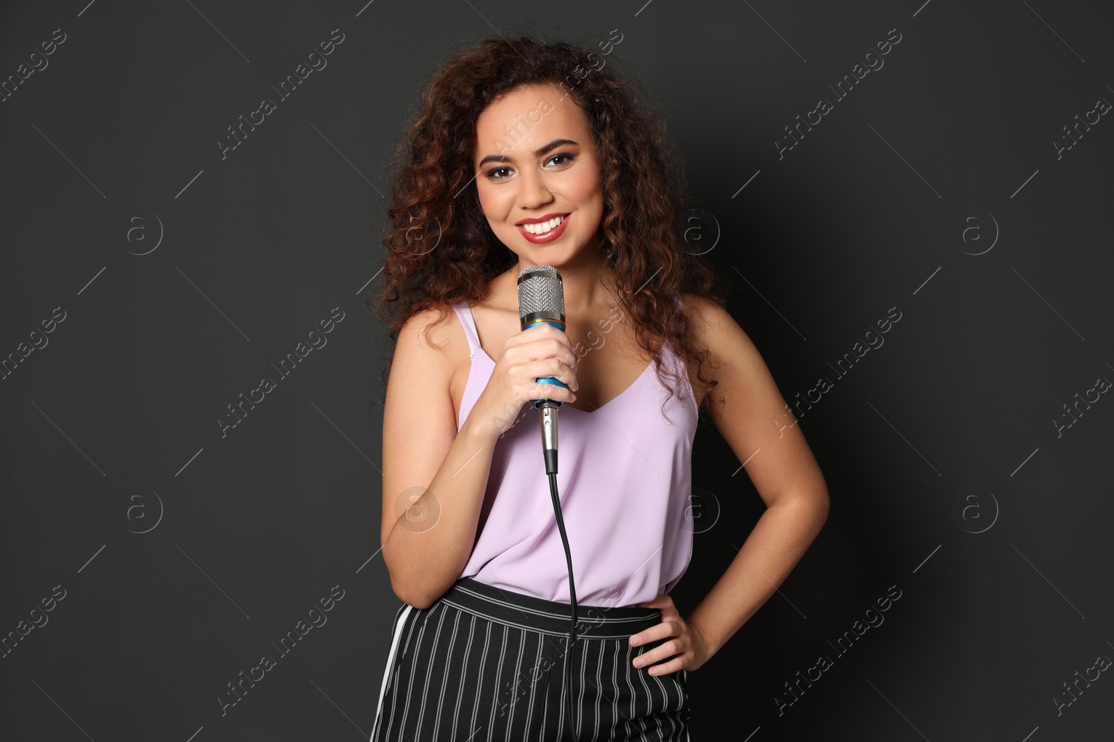 Photo of Curly African-American woman in stylish clothes posing with microphone on black background