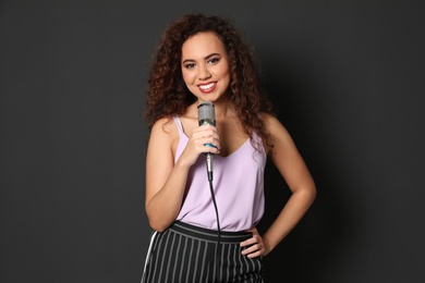 Curly African-American woman in stylish clothes posing with microphone on black background