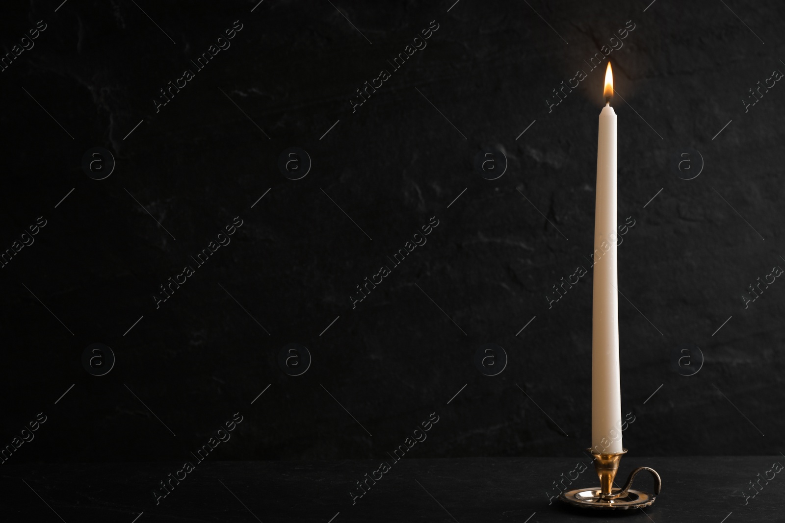 Photo of Elegant candlestick with burning candle on black table. Space for text