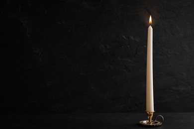 Elegant candlestick with burning candle on black table. Space for text