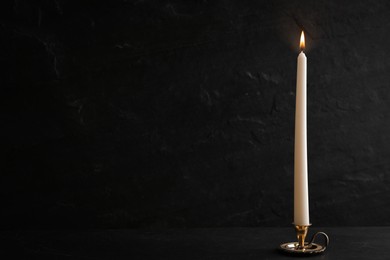 Photo of Elegant candlestick with burning candle on black table. Space for text