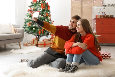 Photo of Happy young couple taking selfie in decorated for Christmas room