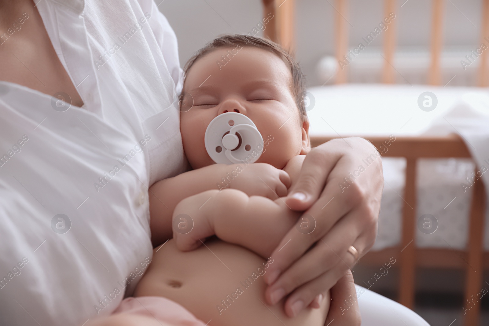 Photo of Mother holding her cute little baby with pacifier at home, closeup