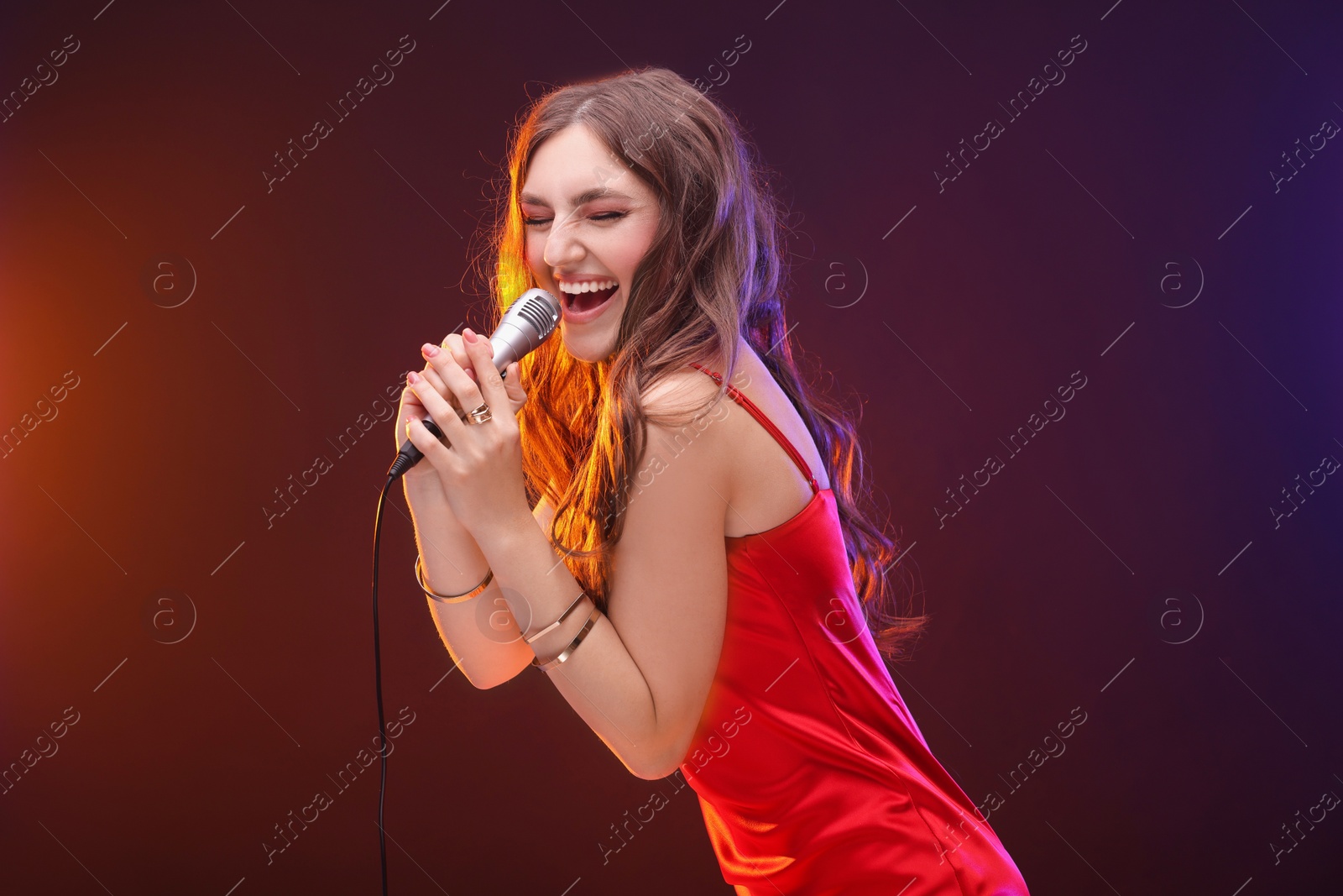 Photo of Emotional woman with microphone singing in color lights