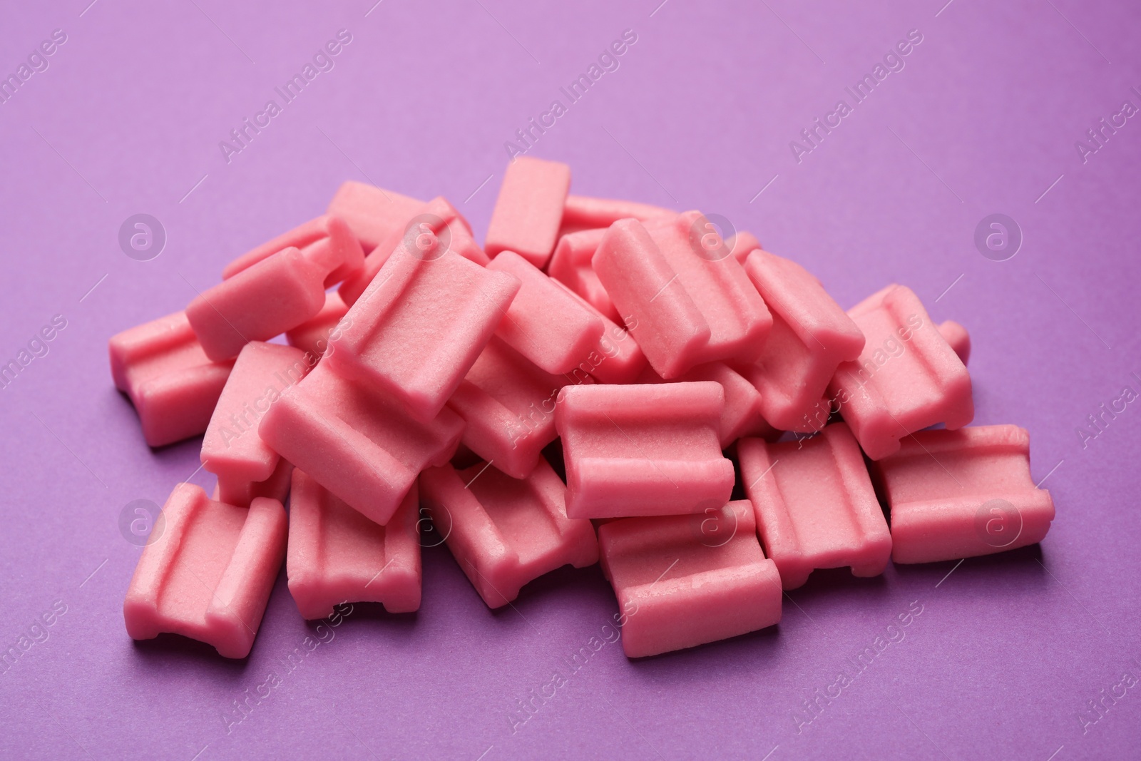 Photo of Tasty pink chewing gums on purple background, closeup